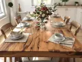 Une table en bois rustique est dressée pour un repas, avec des assiettes, des bols, des verres et un bouquet de fleurs.