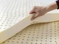 Une main soulève une couche de **latex matière** perforée, révélant sa texture aérée et souple.