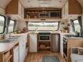 Cuisine de caravane rénovée : plans de travail en bois, évier double, plaques de cuisson, four, réfrigérateur et rangements. Idées pour comment refaire l'intérieur d'une caravane.