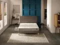 Un lit moderne avec un matelas blanc et un sommier gris, sur un tapis géométrique. Le prix moyen d'un bon matelas est un investissement pour le confort.