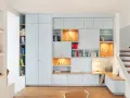 Aménagement d'un **pièce à vivre** moderne avec bibliothèques modulables, rangements intégrés et un banc cosy près de l'escalier.
