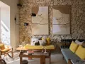 Salon avec mur en pierre, deux tapisseries texturées, fauteuil en rotin, banquette jaune et coussins aux motifs ethniques. Une ambiance deco campagne boheme chaleureuse.