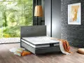 Un lit moderne avec un matelas de dimension queen size, des coussins colorés et une couverture orange sur un parquet en bois.