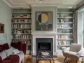Un canapé au milieu du salon, entouré de bibliothèques remplies de livres, d'une cheminée et d'un fauteuil confortable.