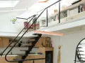 Aménagement mezzanine ouverte avec escalier métallique, cuisine en bois, étagères remplies de livres et plantes suspendues.