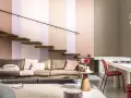 Un confortable canapé en cuir marron est installé sous un escalier flottant en bois. La pièce est décorée de coussins roses et d'un tapis en jute.