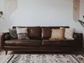 Un canapé marron en cuir, décoré de coussins texturés. Idéal pour savoir quelle couleur associer avec un canapé marron, avec des plantes vertes et un tapis ethnique.