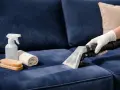 Nettoyer tache canapé velours : un aspirateur extrait la saleté d'un tissu bleu. Brosse, serviette et spray à proximité.
