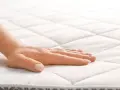 Main d'une femme effleurant un matelas orthopédique, offrant un confort et un soutien idéaux pour un sommeil réparateur.