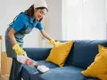 Femme nettoyant un canapé bleu avec un aspirateur pour éliminer la mauvaise odeur du tissu.