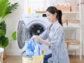 Une femme charge du linge bleu dans une machine à laver. Le cycle de rincage de la machine à laver est terminé.