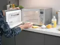 Une personne nettoie un mini four très encrassé avec une éponge. Des citrons, du bicarbonate et du liquide vaisselle sont à proximité.