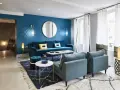 Salon moderne avec mur bleu canard, canapé velours, fauteuils et tapis assortis. Le jaune vif des coussins dynamise l'ensemble.