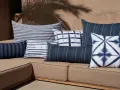 Idée déco plaid sur canapé : coussins bleus et blancs aux motifs rayés et tie-dye sur un canapé de jardin.