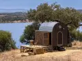 Une caravane transformée en cabane insolite, avec une terrasse en bois, au bord d'un lac paisible.