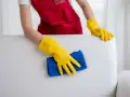 Mains gantées de jaune nettoient un canapé en cuir blanc, redonnant son éclat à ce meuble autrefois très sale.
