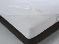 Un matelas blanc avec une alèse imperméable soulevée, montrant de quel côté mettre une alèse pour protéger le matelas.