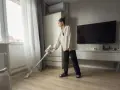 Une femme utilise un aspirateur sans fil, peut-être pour savoir quel est l'aspirateur le plus silencieux.