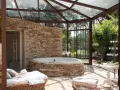 Un spa dans une cave, avec un jacuzzi en pierre, une banquette et une verrière donnant sur un jardin luxuriant.