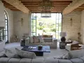 L'intérieur d'un mas provençal baigné de lumière, avec des poutres apparentes, des murs en pierre et une vue imprenable sur la campagne.