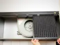 Mains d'une personne retirant un filtre à charbon d'une hotte aspirante pour le nettoyer.