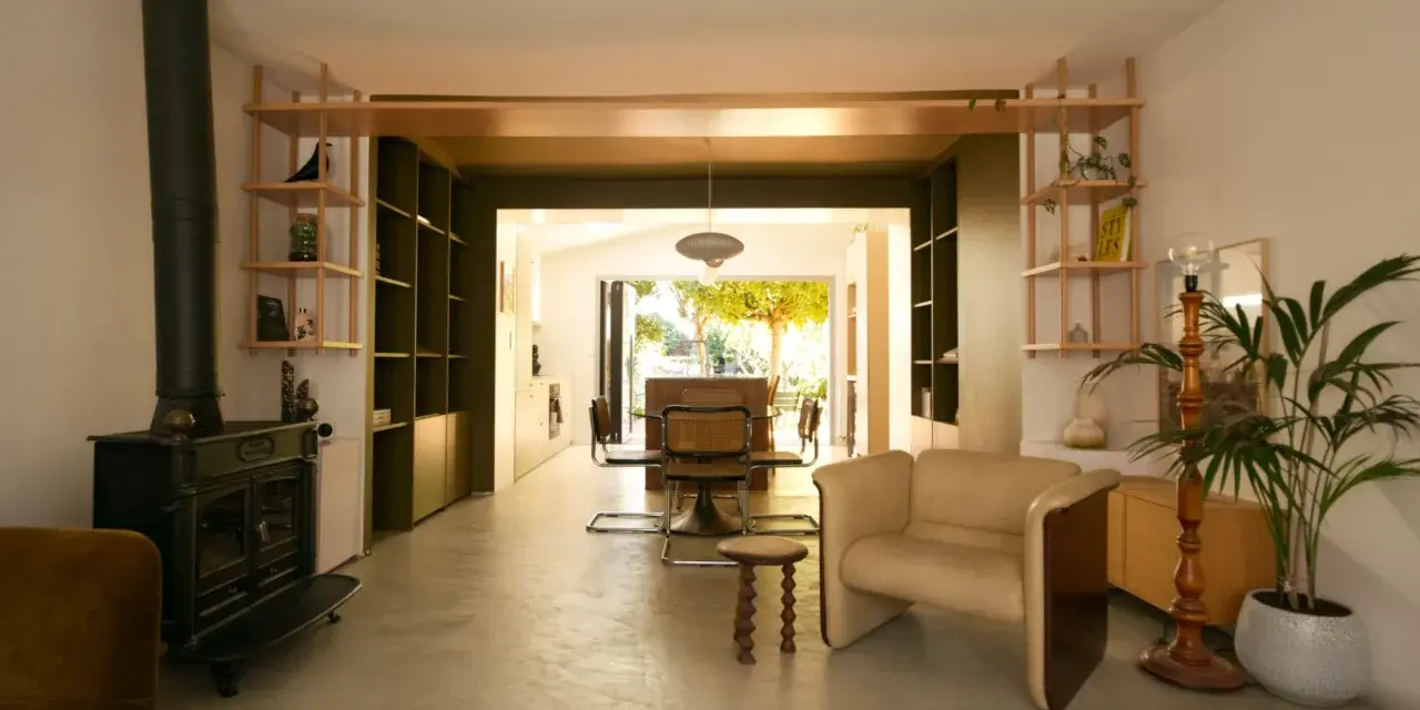 Aménagement maison en longueur : salon avec poêle, étagères et vue sur salle à manger et jardin.