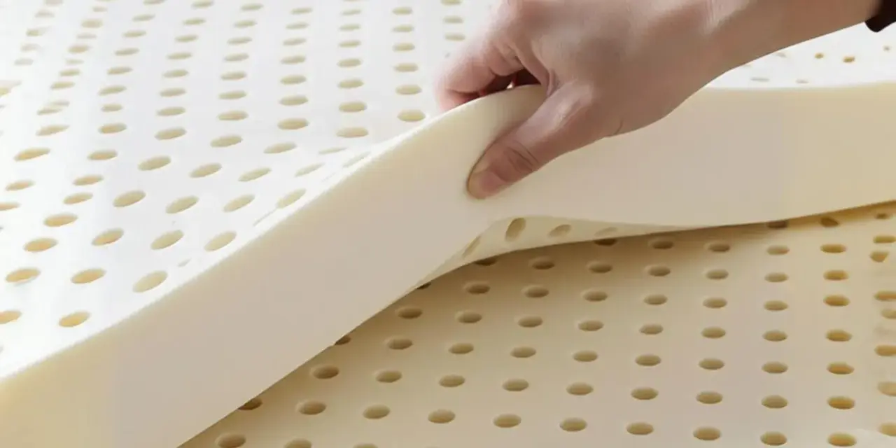 Une main soulève une couche de **latex matière** perforée, révélant sa texture aérée et souple.