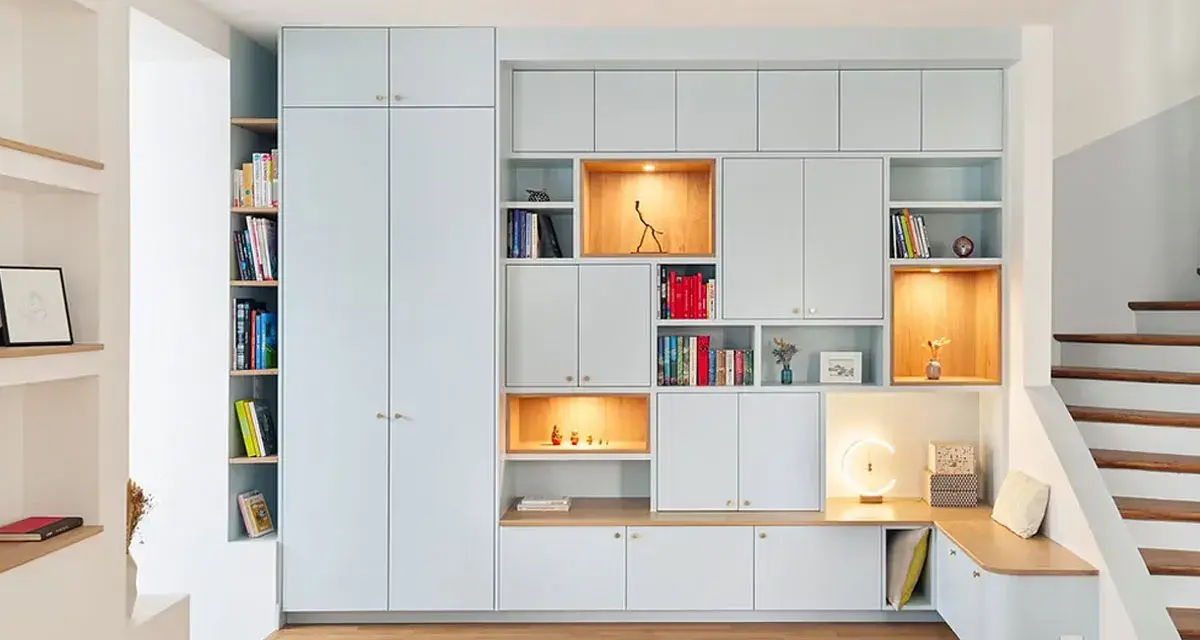 Aménagement d'un **pièce à vivre** moderne avec bibliothèques modulables, rangements intégrés et un banc cosy près de l'escalier.