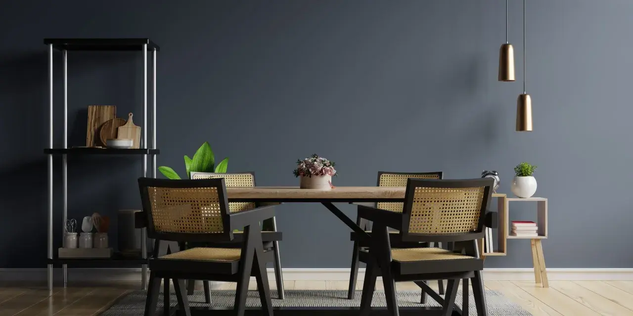 Salle à manger moderne avec chaises en rotin et table en bois. Deux suspensions dorées au-dessus, une étagère noire à gauche. Idées pour comment éclairer une pièce sombre.