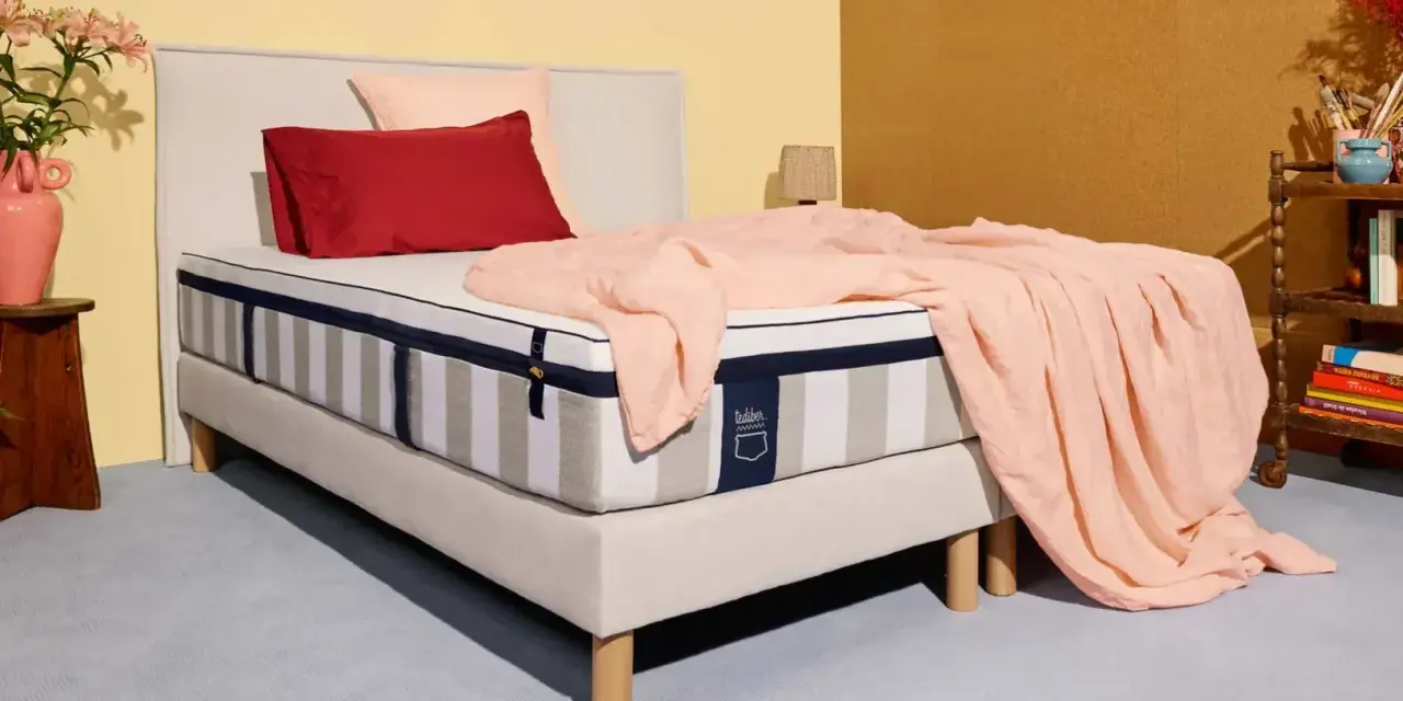 Un matelas rayé, drapé d'une couverture rose pâle, avec des coussins rouge et rose. La question est : combien de ressorts pour un bon matelas ?