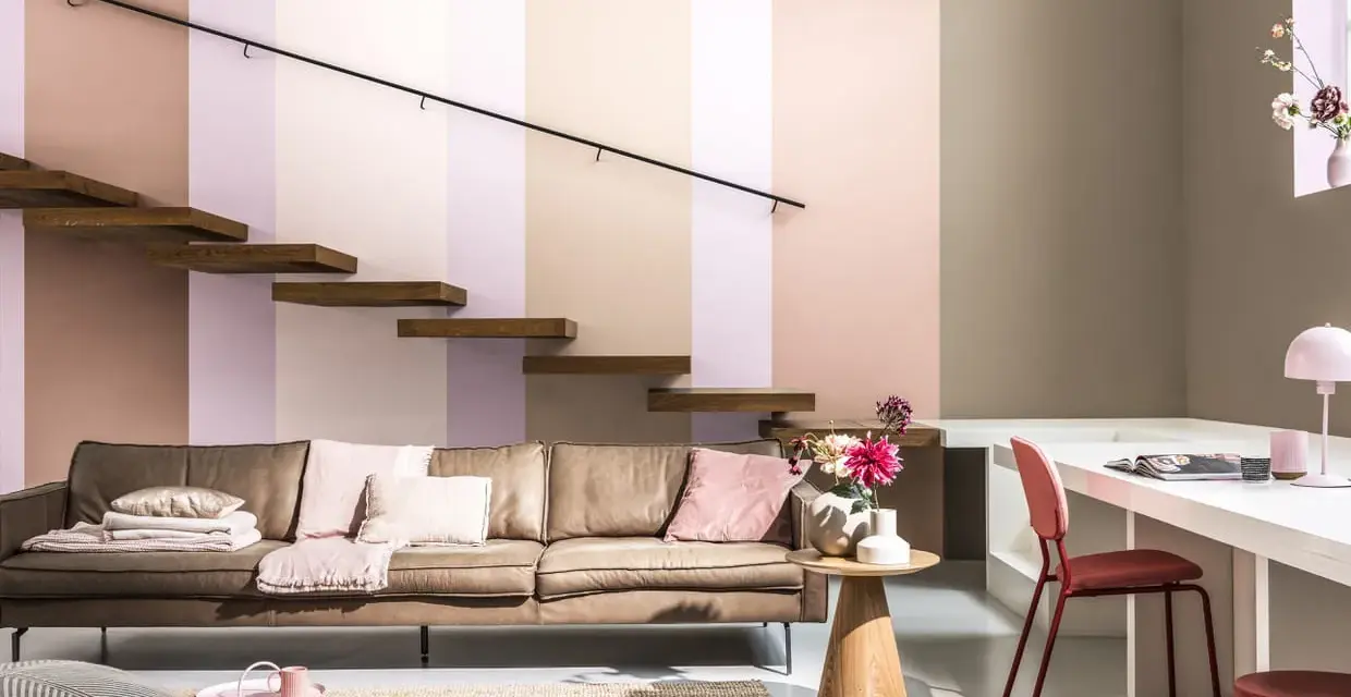 Un confortable canapé en cuir marron est installé sous un escalier flottant en bois. La pièce est décorée de coussins roses et d'un tapis en jute.