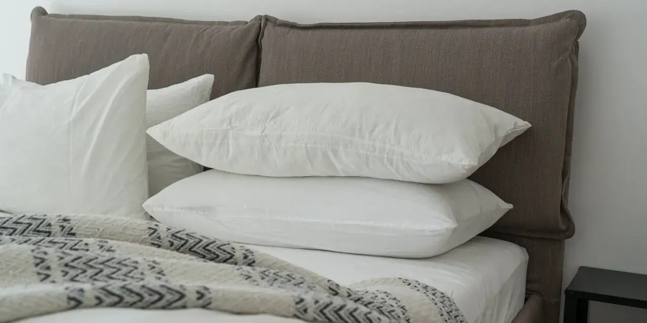 Lit douillet avec deux oreillers blancs empilés, une couverture à motifs et un drap housse ou protège matelas immaculé.