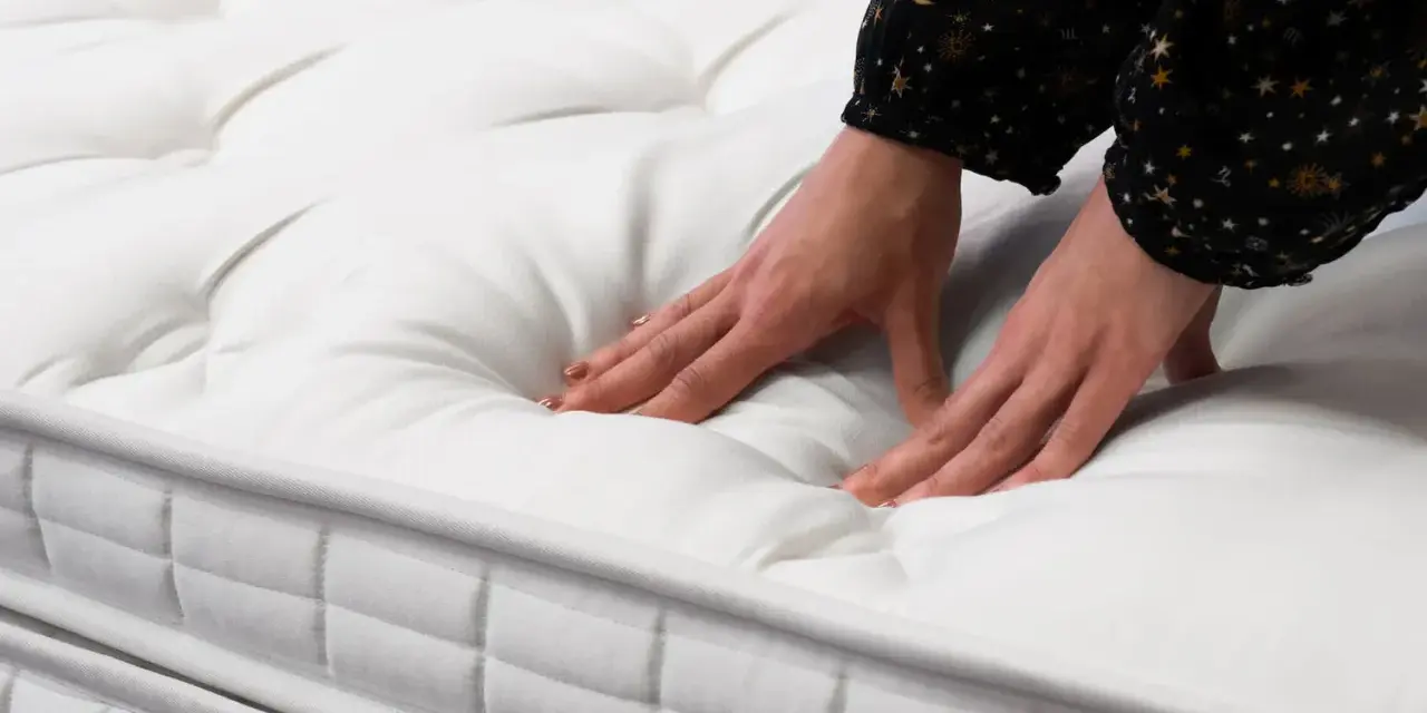 Mains testant la douceur d'un matelas blanc matelassé. Quel matelas pour mal de dos dur ou mou ? Le confort est essentiel.