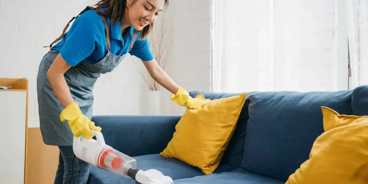 Femme nettoyant un canapé bleu avec un aspirateur pour éliminer la mauvaise odeur du tissu.