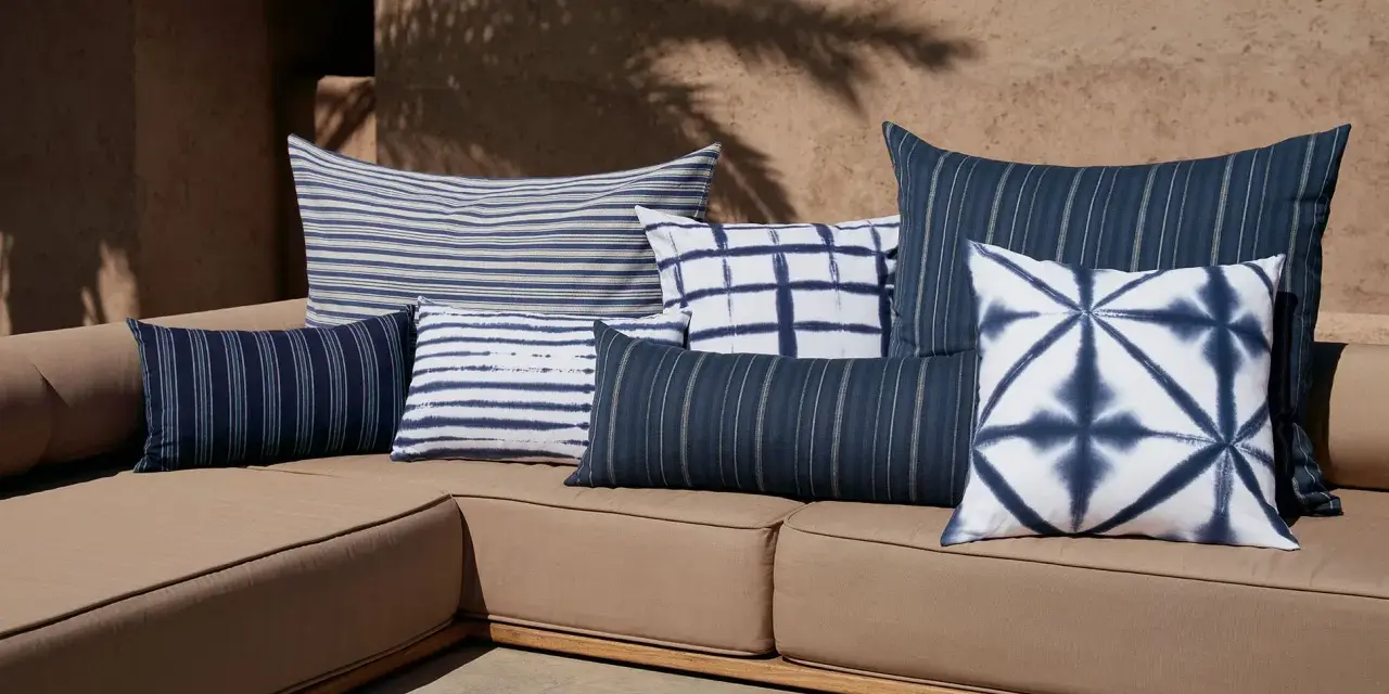 Idée déco plaid sur canapé : coussins bleus et blancs aux motifs rayés et tie-dye sur un canapé de jardin.