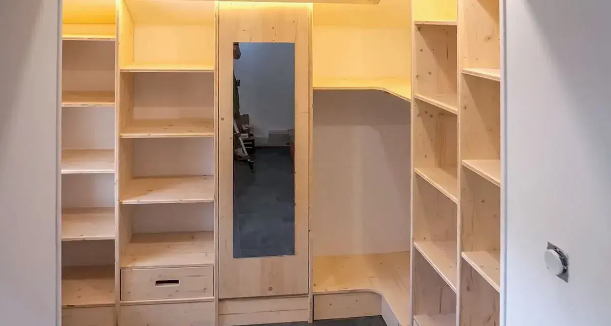 Construction d'une armoire sur mesure avec des portes coulissantes et des étagères en bois clair. Un miroir est intégré.