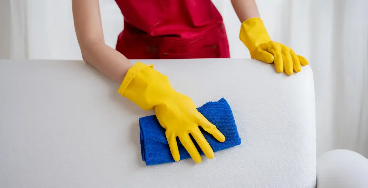 Mains gantées de jaune nettoient un canapé en cuir blanc, redonnant son éclat à ce meuble autrefois très sale.
