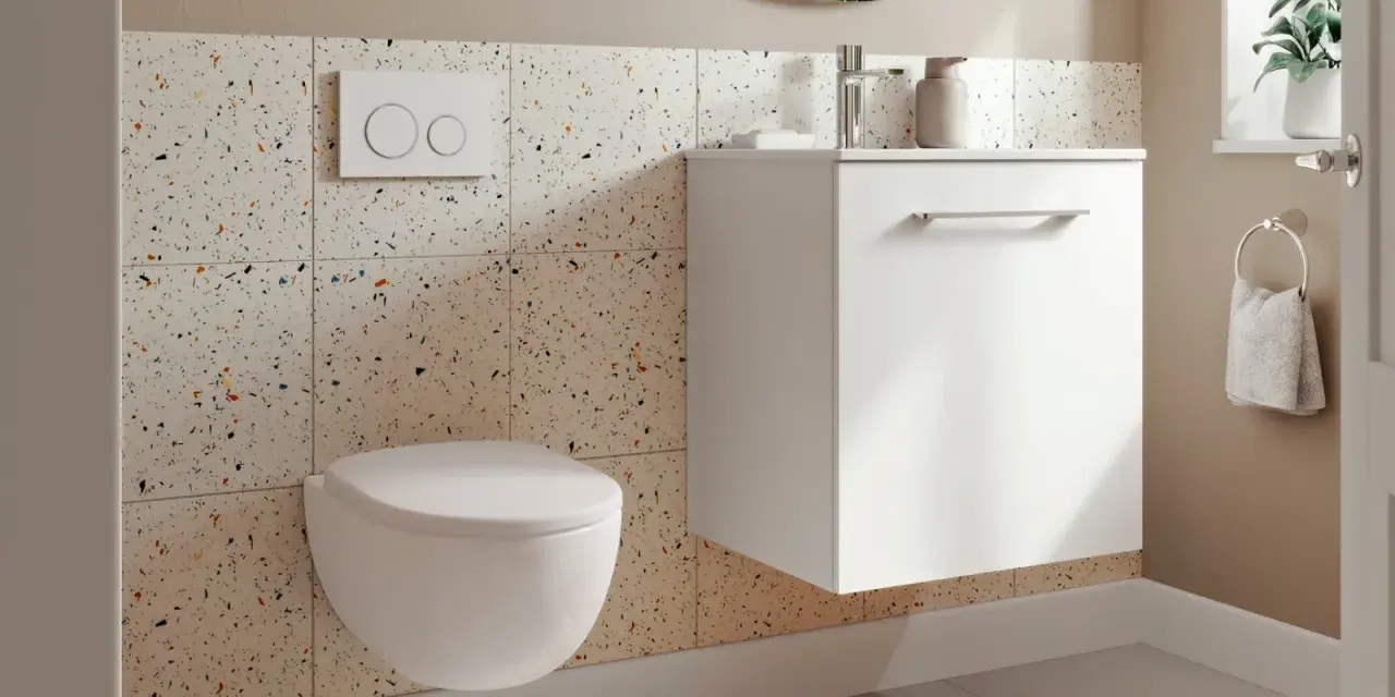 Une petite toilette moderne suspendue, avec un mur en carreaux de terrazzo colorés et un meuble blanc flottant.