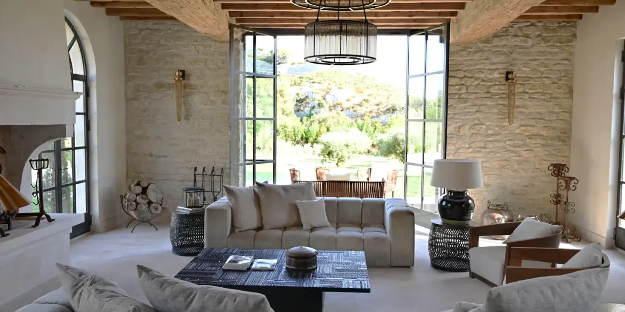 L'intérieur d'un mas provençal baigné de lumière, avec des poutres apparentes, des murs en pierre et une vue imprenable sur la campagne.