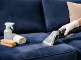 Nettoyer tache canapé velours : un aspirateur extrait la saleté d'un tissu bleu. Brosse, serviette et spray à proximité.
