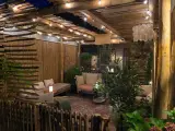 Une terrasse de jardin aménagée en coin cocooning, avec des banquettes confortables, des lumières douces et une ambiance chaleureuse.