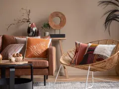 Un salon cosy avec un canapé en cuir marron, des coussins aux motifs ethniques et une chaise en rotin.