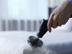 Main d'une personne utilisant un nettoyeur vapeur pour nettoyer un matelas en mousse. Une méthode efficace pour savoir comment nettoyer un matelas en mousse.