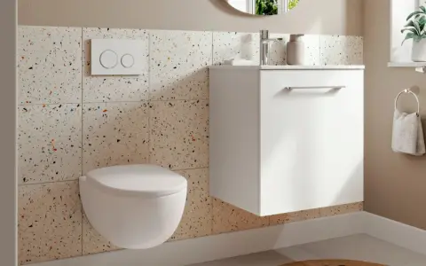 Une petite toilette moderne suspendue, avec un mur en carreaux de terrazzo colorés et un meuble blanc flottant.