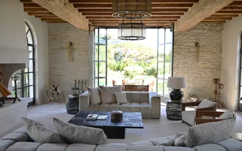 L'intérieur d'un mas provençal baigné de lumière, avec des poutres apparentes, des murs en pierre et une vue imprenable sur la campagne.