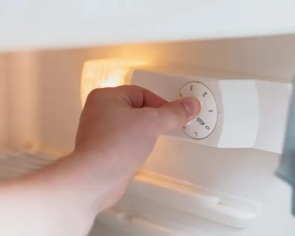 Main tenant ajuste la molette pour régler la quelle temperature congelateur. Le bouton indique "STOP" et des chiffres de 0 à 7.
