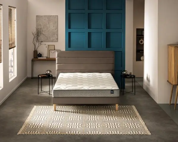 Un lit moderne avec un matelas blanc et un sommier gris, sur un tapis géométrique. Le prix moyen d'un bon matelas est un investissement pour le confort.