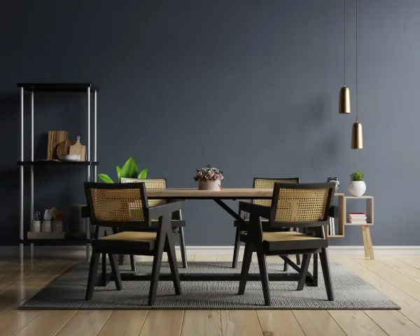Salle à manger moderne avec chaises en rotin et table en bois. Deux suspensions dorées au-dessus, une étagère noire à gauche. Idées pour comment éclairer une pièce sombre.