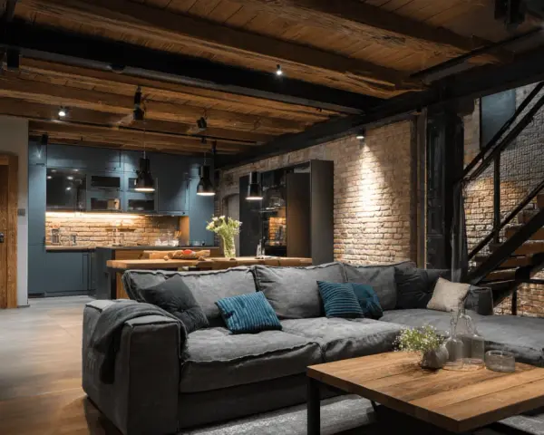 Un salon cosy avec un grand canapé gris, une cuisine moderne et un escalier industriel. Idéal pour aménager un souplex avec style.
