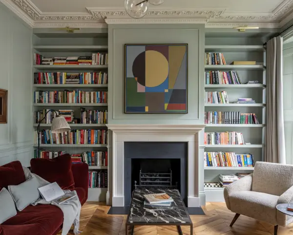 Un canapé au milieu du salon, entouré de bibliothèques remplies de livres, d'une cheminée et d'un fauteuil confortable.